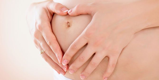 Kobieta w ciąży obejmuje brzuch rękami, tworząc kształt serca