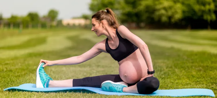 Ćwiczenia fitness kobiety w ciąży na macie, na trawie w słoneczny dzień