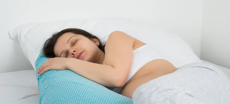 Młoda kobieta w ciąży śpi w sypialni na łóżku z ręką na kołdrze