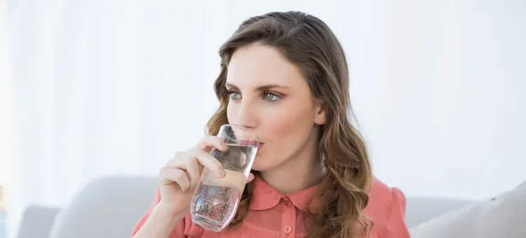 Kobieta ciężarna siedząca na kanapie pije wodę ze szklanki