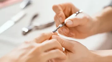 Specjalistka od manicure trzyma dłoń klientki i używa szpatułki do skórek, wykonując manicure w salonie