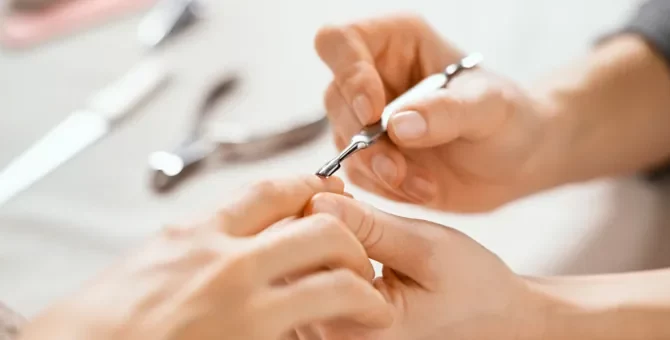 Specjalistka od manicure trzyma dłoń klientki i używa szpatułki do skórek, wykonując manicure w salonie