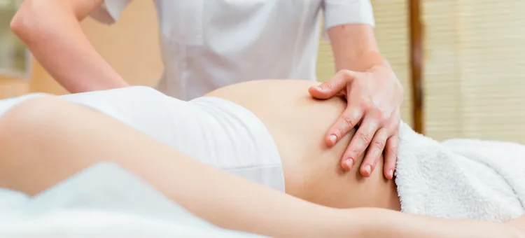 Ręce terapeutki wykonują delikatny masaż brzucha kobiety w ciąży na stole w gabinecie kosmetycznym
