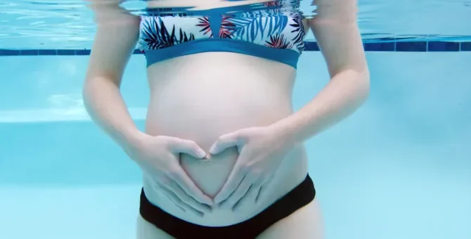 Ciało kobiety w ciąży, w basenie, rece w kształcie serca na brzuchu