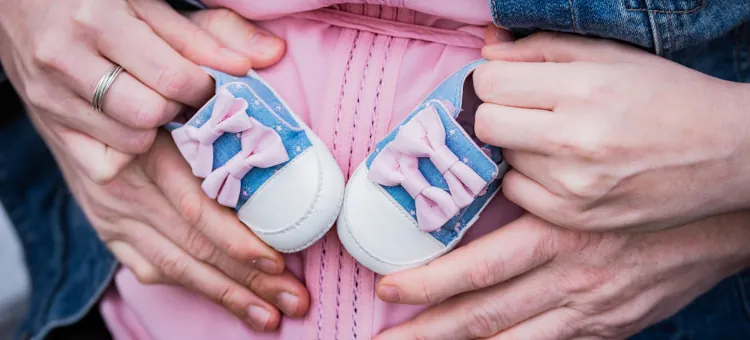 Ręce przyszłej mamy i ojca trzymają dziecięce buciki dla przyszłego dziecka, obejmując brzuch kobiety