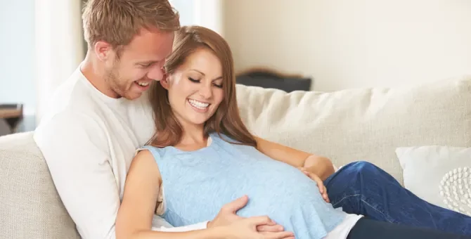 Kobieta w ciąży relaksująca się na kanapie z mężczyzną, dotykają brzucha kobiety
