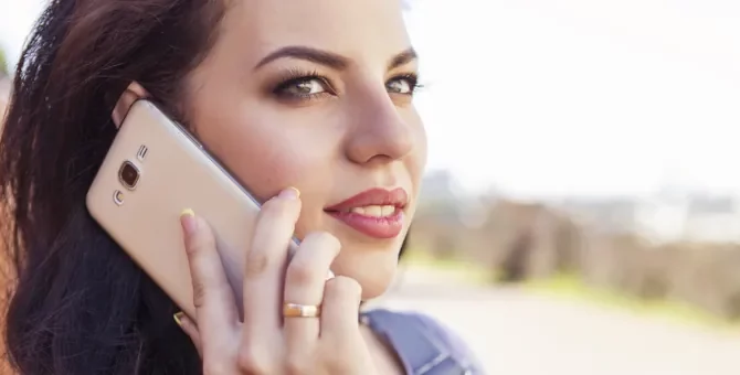 Ciemnowłosa kobieta w ciąży rozmawia przez telefon na dworze