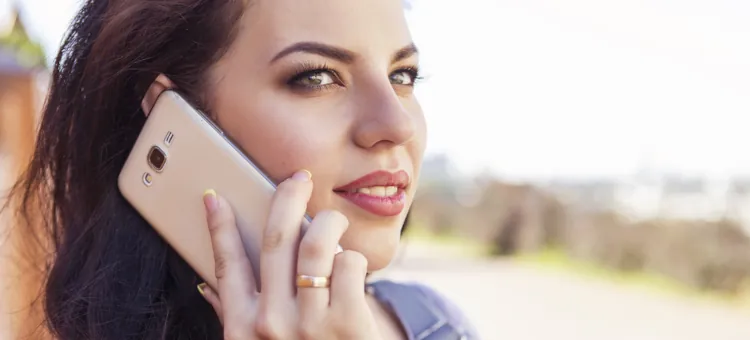 Ciemnowłosa kobieta w ciąży rozmawia przez telefon na dworze