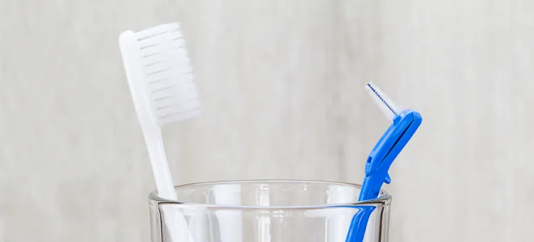 Szczoteczka do zębów i szczoteczka międzyzębowa w szklance na rozmytym tle w łazience