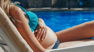 Kobieta w ciąży odpoczywa na leżaku przy basenie i wystawia brzuch na słońce