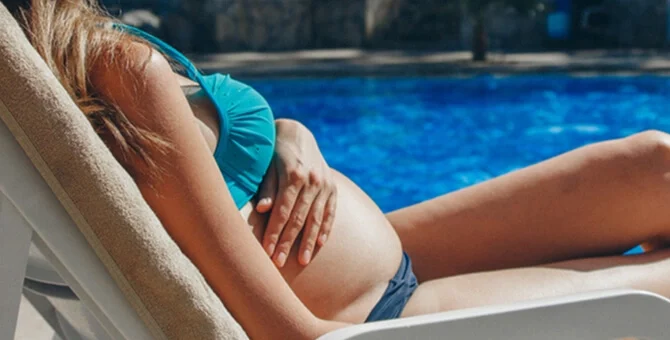 Kobieta w ciąży odpoczywa na leżaku przy basenie i wystawia brzuch na słońce