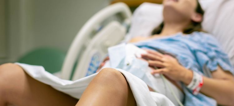 Kobieta rodząca, z bolesnymi skurczami, leżąca w szpitalnym łóżku.