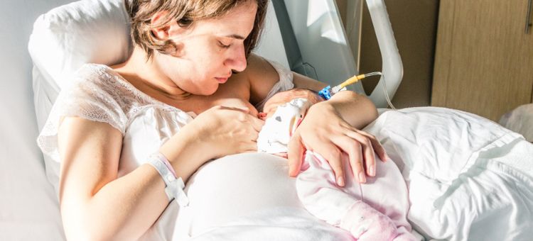 Matka ostrożnie karmi piersią swoją nowo narodzoną córeczkę w szpitalnym łóżku