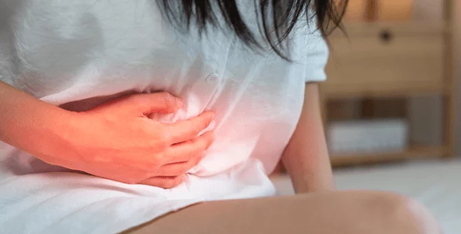 Kobieta trzymająca się za podbrzusze z powodu bólu po porodzie, który może wskazywać na zapalenie błony śluzowej macicy.