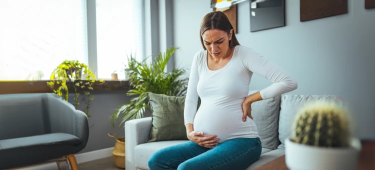 Kobieta w ciąży z bólem brzucha z rękami na brzuchu i plecach.