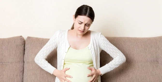 Kobieta w ciąży z zaparciem z rękami na brzuchu