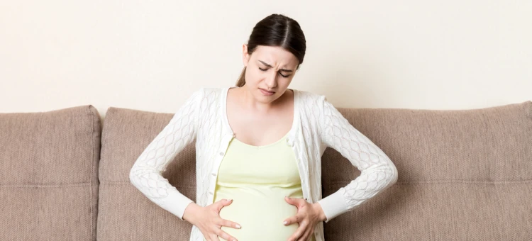 Kobieta w ciąży z zaparciem z rękami na brzuchu