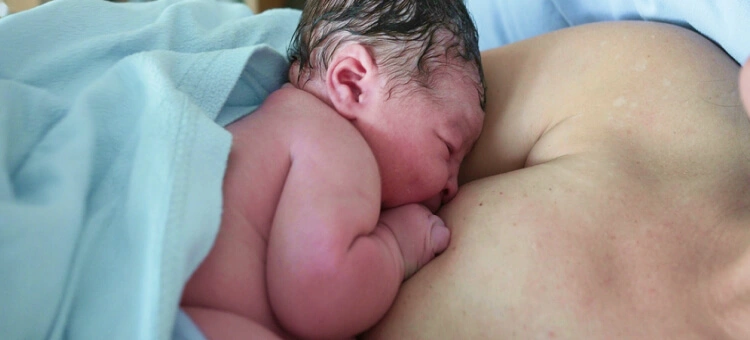 Noworodek pijący mleko z piersi matki tuż po porodzie