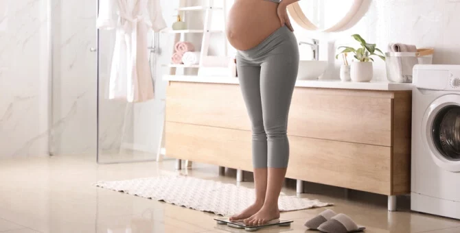 Kobieta w ciąży ważąca się na wadze w łazience