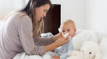 Mama wycierająca nos małemu dziecku leżącemu w łóżku