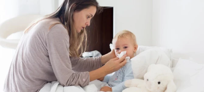 Mama wycierająca nos małemu dziecku leżącemu w łóżku