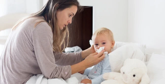 Mama wycierająca nos małemu dziecku leżącemu w łóżku