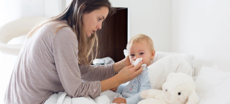 Mama wycierająca nos małemu dziecku leżącemu w łóżku