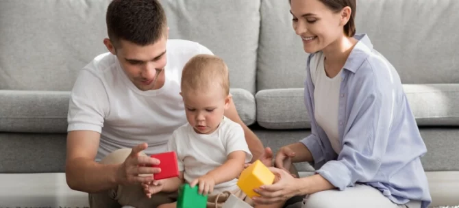 Mama i tata bawiący się z rocznym dzieckiem na dywanie.