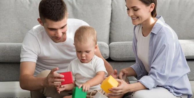 Mama i tata bawiący się z rocznym dzieckiem na dywanie.