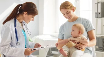 Mama z niemowlęciem podczas wizyty u pediatry – lekarz uzupełnia książeczkę zdrowia dziecka