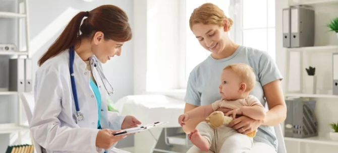 Mama z niemowlęciem podczas wizyty u pediatry – lekarz uzupełnia książeczkę zdrowia dziecka