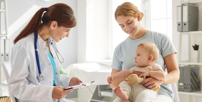 Mama z niemowlęciem podczas wizyty u pediatry – lekarz uzupełnia książeczkę zdrowia dziecka