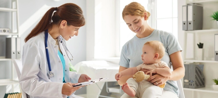 Mama z niemowlęciem podczas wizyty u pediatry – lekarz uzupełnia książeczkę zdrowia dziecka