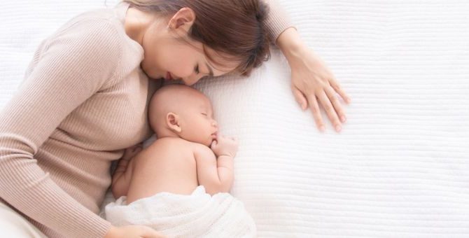 Obraz radosnej matki, która delikatnie tuląc, trzyma swoje śpiące maleństwo w ramionach.