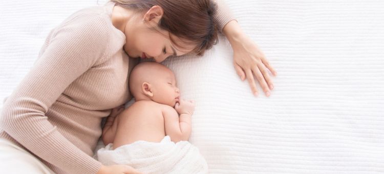 Obraz radosnej matki, która delikatnie tuląc, trzyma swoje śpiące maleństwo w ramionach.