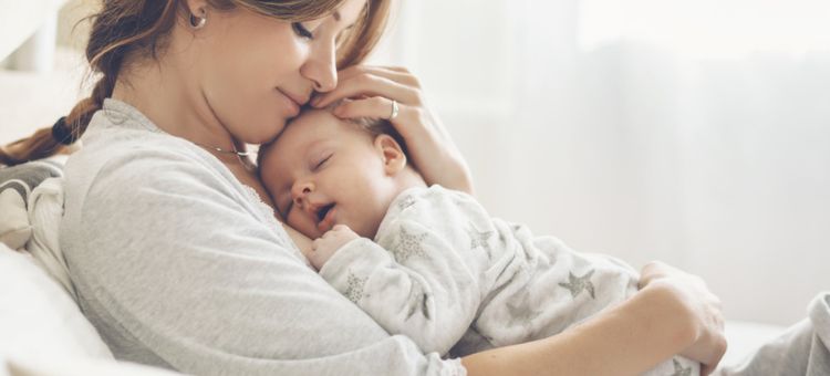 Jasny portret szczęśliwej mamy trzymającej śpiące dziecko w ramionach.
