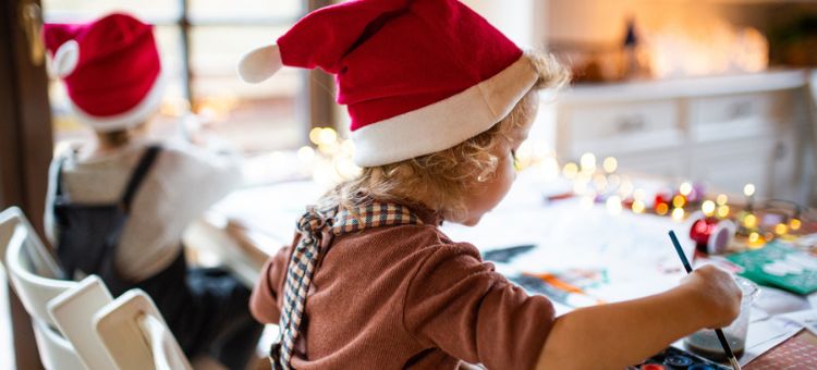 Dziecko w czapce Świętego Mikołaja maluje świąteczny obrazek