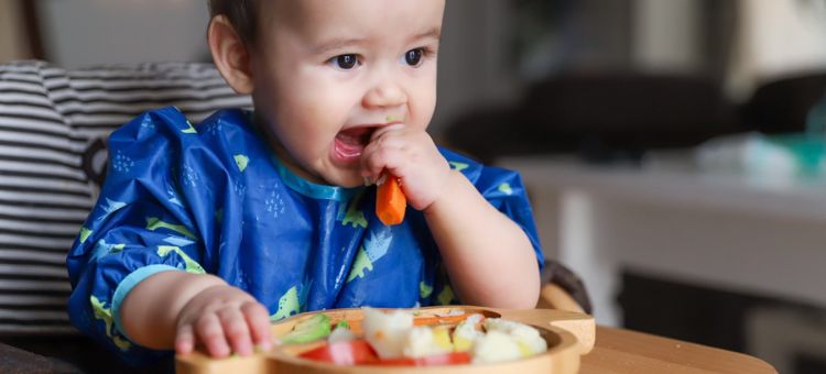Dziecko w niebieskim ubranku jedzące samodzielnie marchewkę