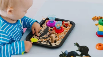 Dziecko bawiące się ziarnami i figurkami na tacy sensorycznej