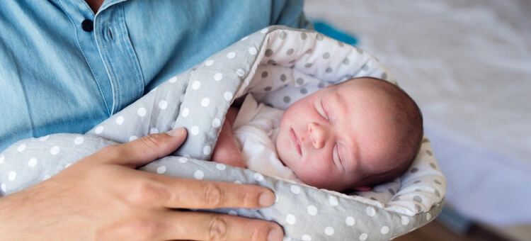 Śpiący noworodek trzymany bezpiecznie na rękach rodzica, z podparciem całego ciała