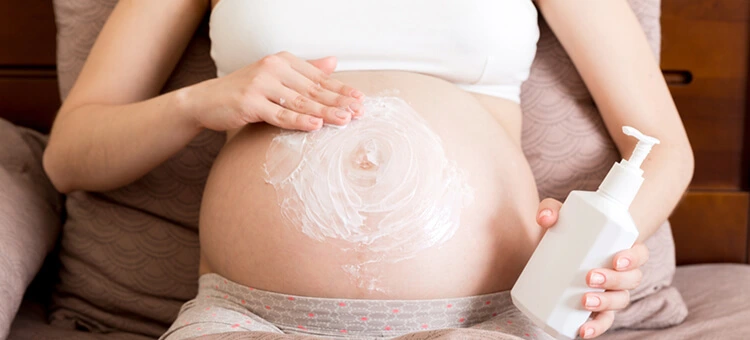 Jak pielęgnować kresę czarną na brzuchu w ciąży? Kobieta w ciąży z linea negra nakładająca krem na skórę brzucha