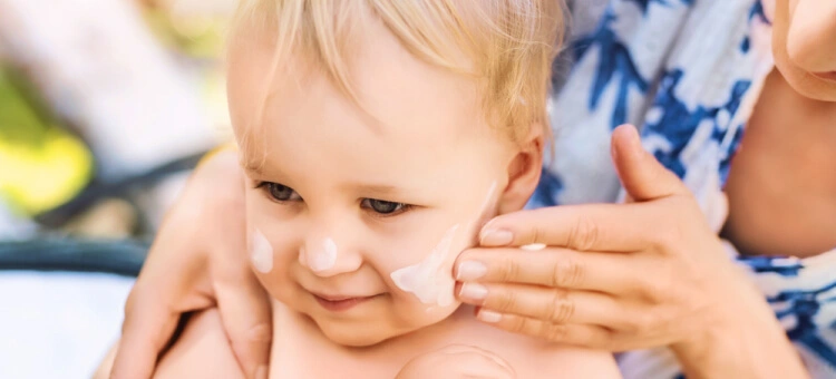 Mama kremująca twarz kremem przeciwsłonecznym dziecku