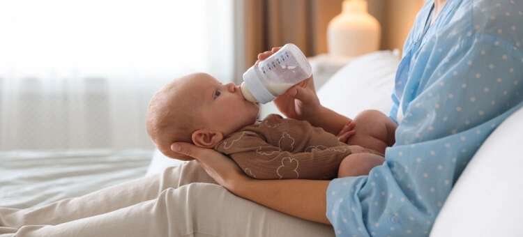 Karmienie niemowlaka butelką trzymaną przez mamę w pozycji karmienia na udach