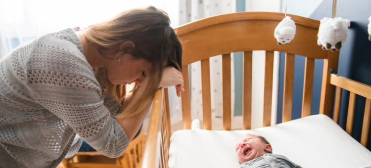 Noworodek płaczący przez sen w łóżeczku a obok mama