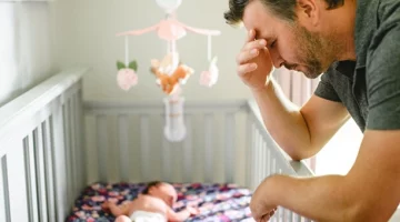 Zmęczony ojciec siedzący przy łóżeczku niemowlęcia