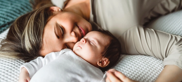 Niemowlę leżące z mamą na łóżku