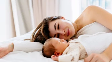 Wspólne spanie z niemowlęciem – mama leży obok maluszka na łóżku i patrzy na niego