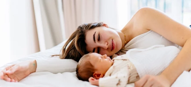 Wspólne spanie z niemowlęciem – mama leży obok maluszka na łóżku i patrzy na niego