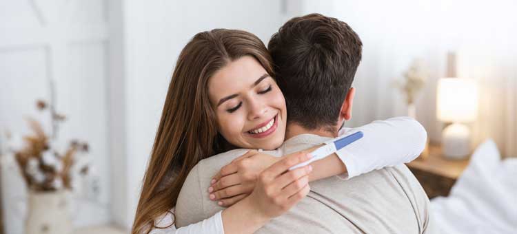 Szczęśliwa kobieta z pozytywnym wynikiem testu ciążowego przytulająca się do partnera