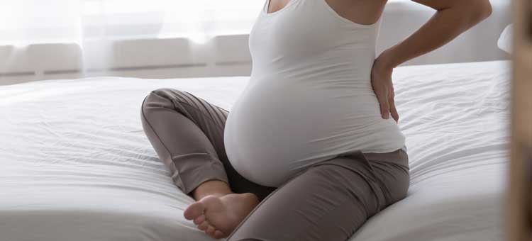 Kobieta w ciąży na łóżku obejmuje swój brzuch